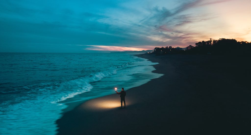 Image of a man with a torch on a beach looking out into the ocean. The emphasis is looking into the unknown, which is how roth conversions can feel.